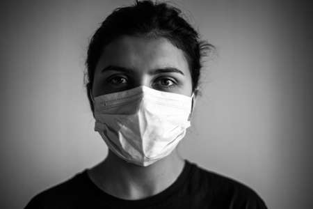 Monochrome portrait of a young woman wearing medical mask. Dramatic black and white closeup of a girl being protected from coronavirus and flu illness with sterile mask. Quarantine stay home conceptの写真素材