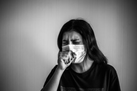Portrait of a young woman wearing medical sterile mask, coughs and covers with her hands. Dramatic black and white closeup of a girl being protected from coronavirus. Quarantine stay home conceptの写真素材