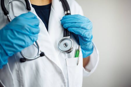 Closeup of a woman doctor wearing white medical gown and blue gloves, stethoscope. Female nurse holding a stethoscope on her neck. Coronavirus, nCov2019, covid-19 and sickness prevention conceptの写真素材