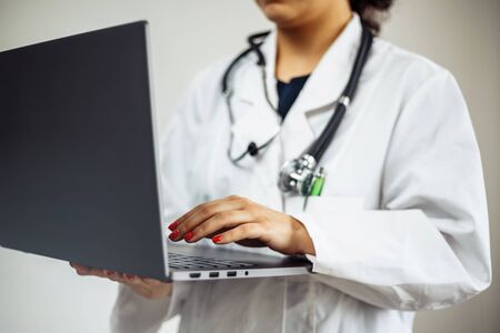 Closeup of a woman doctor wearing white medical gown and blue gloves, stethoscope. Female nurse holding a laptop in her hands. Coronavirus, covid-19 and sickness prevention conceptの写真素材