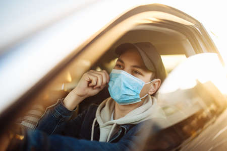 A boy drives a car fits and adjusts medical sterile mask during coronavirus pandemic quarantine. Man...