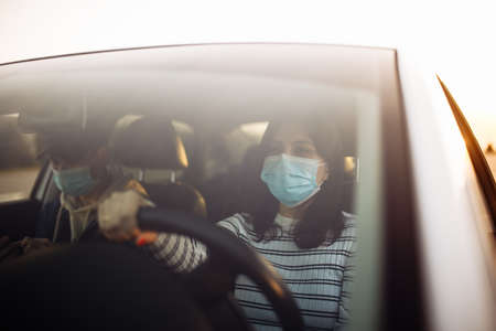 Boy and girl driving a car wearing sterile medical mask. Taxi driver with a passanger stuck in a traffic jam during coronavirus quarantine isolation in the city. Prevernt spread of covid-19 conceptの写真素材