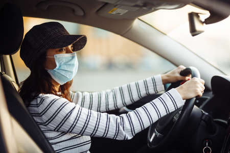 Woman car driver rides wearing medical sterile mask during pandemic coronavirus quarantine. Transport isolation to stop spread of virus of covid-19. Healthcare conceptの写真素材