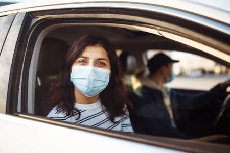 A girl and a boy driving in a car during coronavirus quarantine wearing medical masks. Safe taxi and healthcare during pandemic covid-19. Passangers virus safety conceptの写真素材
