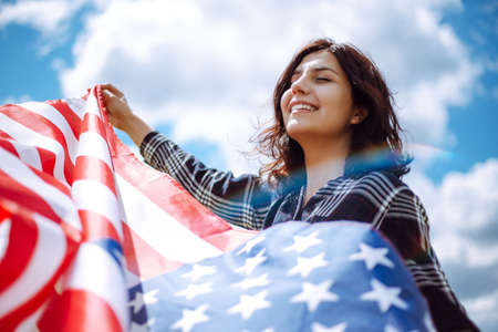 Patriotic young woman wrapped in an american flag on a beautiful field with yellow flowers. USA...
