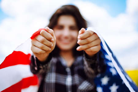Closeup of hands of a patriotic young woman wrapped in an american flag on a beautiful field with yellow flowers. USA independence day 4th of July celebration. Summer holidays conceptの写真素材