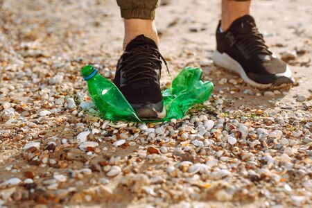 Young male volunteer picks up plastic garbage on the ocean coast. A man collects waste on the seaside to save ecology and protect environment. Recycle litter and pollution conceptの写真素材
