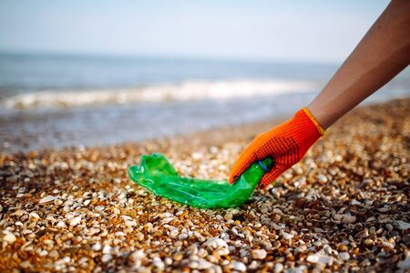 Closeup of young male volunteer's hands picks up plastic garbage on the ocean coast. A man collects waste on the seaside to save ecology and protect environment. Recycle litter and pollution conceptの写真素材