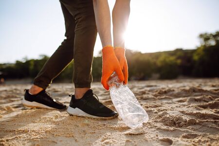 Young male volunteer picks up plastic garbage on the ocean coast. A man collects waste on the seaside to save ecology and protect environment. Recycle litter and pollution conceptの写真素材