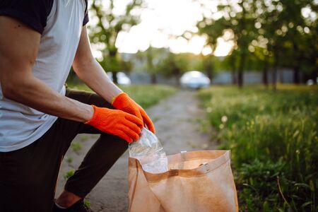 Young man volunteer picks up trash at the park. Plastic bottle is being collected by the man wearing...