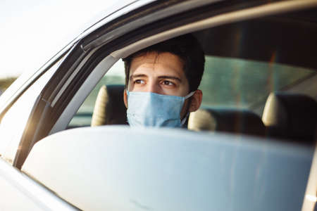 Young businessman takes a taxi and looks out of the car window wearing sterile medical mask. A man...