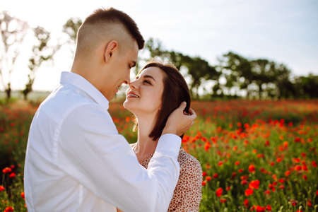 Romantic young couple hug among red beautiful poppy field. Loving boy and girl stand, hug and kiss showing their feelings to each other. Freedom, wedding, family and love conceptの写真素材