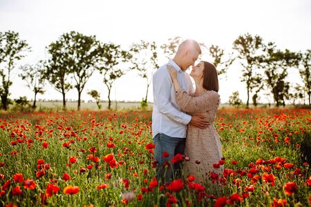 Romantic young couple hug among red beautiful poppy field. Loving boy and girl stand, hug and kiss showing their feelings to each other. Freedom, wedding, family and love conceptの写真素材