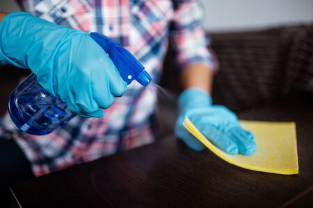 Cleaning dark table surface with spray detergent, blue rubber gloves and yellow dish cloth on work surface. Antibacterial work against coronavirus. Concept for hygiene, disinfection and health careの写真素材
