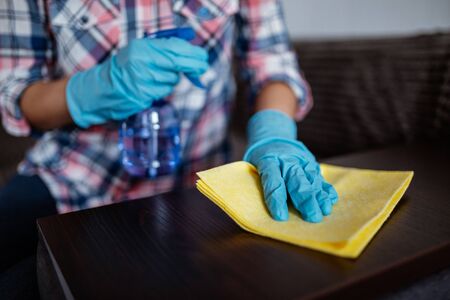 Cleaning dark table surface with spray detergent, blue rubber gloves and yellow dish cloth on work...