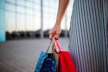 Closeup of young attractive woman holding a few shopping bags with newly purchased goods and clothes. Girl holds colourful packs full of bought things in her hands. Shopping and spendings conceptの写真素材