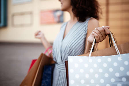 Closeup of young attractive woman holding a few shopping bags with newly purchased goods and clothes. Girl holds colourful packs full of bought things in her hands. Shopping and spendings concept.の写真素材