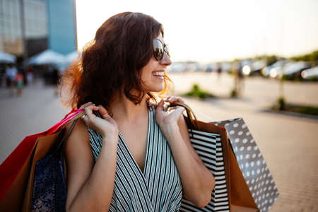 Happy girl stands near boutique shop holding a few bags with purchases. Young woman is glad to buy new clothes during sales season for a reasonable price. Shopping, discount, spend money conceptの写真素材