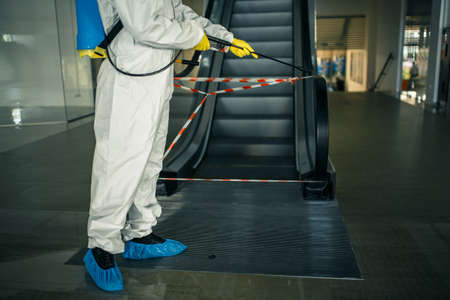Sanitizing worker disinfects the escalator with a spray at the empty shopping mall to prevent the covid-19 spread in public places. Healthcare, clean, isolation and quarantine concept.の写真素材