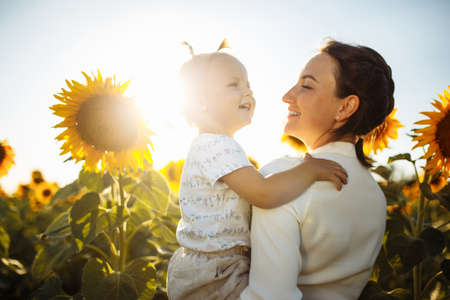 Young mother and her little daughter having fun and enjoy life at the sunflower field on a bright sunny summer day. Summer holiday with family. Happiness, freedom and family values concept.の写真素材