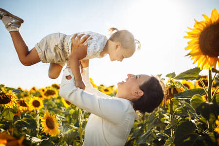 Happy mother with the daughter in the field with sunflowers having fun on a sunny summer day. Family value, unity, happiness, love and joy concept.の写真素材