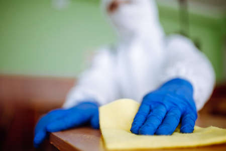 Closeup of a man from disinfection group cleans up the desk at school with a yellow rag. Professional worker sterilizes the classroom to prevent covid-19 spread. Healthcare of pupils and studentsの写真素材