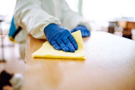 Closeup of a man from disinfection group cleans up the desk at school with a yellow rag....