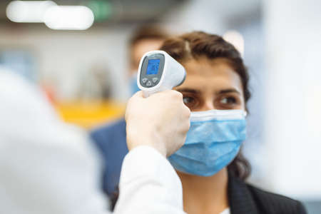 Office workers are checked with a distant non contact thermometer during coronavirus pandemic. Young...