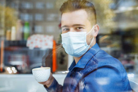 Portrait of a man working from a cafe on a laptop remotely. Businessman leading matters in a distance with a cup of coffee during coronavirus pandemic quarantine. Health care and safety conceptの写真素材