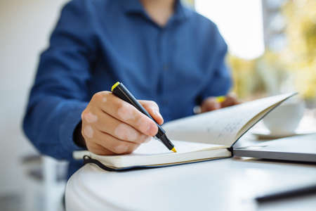 Young man taking noted and working from a cafe during coronavirus pandemic quarantine and staying...