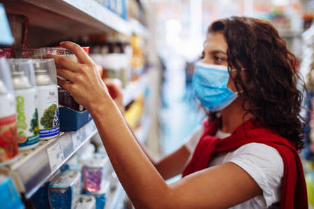 Young woman picks up the disinfecting and cleaning scour at a supermarket wearing a medical sterile mask during the coronavirus pandemic quarantine. Healthcare and home sanitizing conceptの写真素材