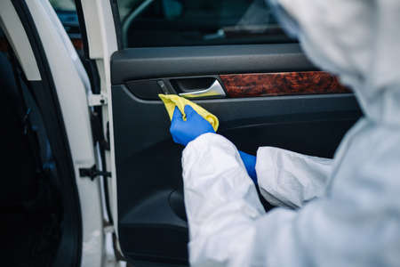 Sanitizing service worker cleans the car's interior with a yellow rug. A man in a protective suit,...