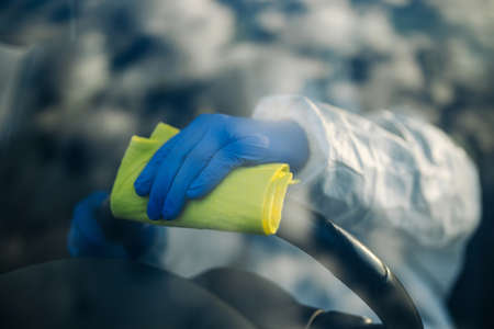 Disinfection professional cleans up a steering wheel of a car with a yellow rug. Sanitary service worker disinfects the vehicle's driver seat place. Covid-19 spread prevention. Health conceptの写真素材