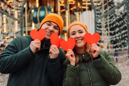 Young happy couple having fun outdoor with red paper hearts at winter season. A boy and a girl love each other and spend time together before Valentines day. Holidays and Christmas conceptの写真素材