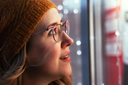 Young woman's portrait at a Christmas market decorated with lights. Female wearing orange hat and...