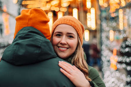 Loving young couple standing together outdoors among garlands at winter season. A boy and a girl having fun, hug and kiss each other in the lights of Christmas market. Holidays conceptの写真素材