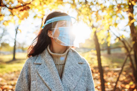 Young woman wearing a face shield to protect from coronavirus desease stands in the park during...