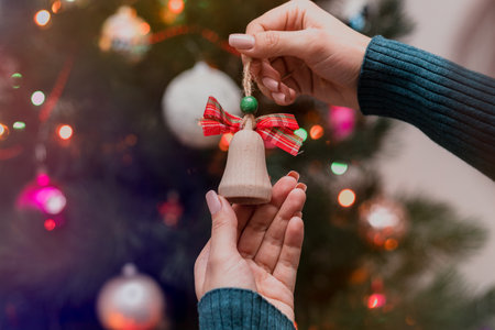 Woman holding christmas tree wooden toy in her hands and hanging it on the Christmas fir tree. Winter holidays lights and garlands. Festive mood conceptの写真素材