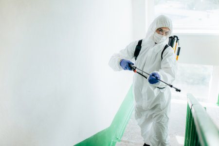 Sanitary professional worker wearing protective suit disinfects a staircase entryway block of flats. Coronavirus prevention measures at residential areas. New normal and stop Covid-19 spread conceptの写真素材