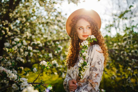 Portrait of a young woman enjoying spring season and standing among blooming trees at the park....