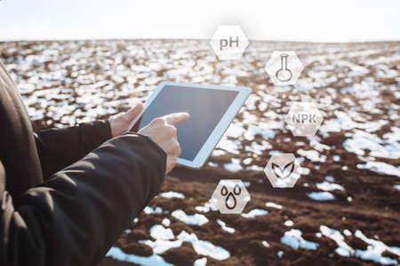 Tablet in the hands of a farmer checking the preparation process and soil readiness for seeding new...