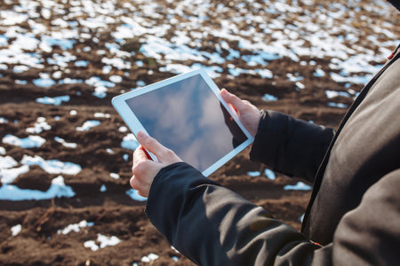 Tablet in the hands of a farmer checking the preparation process and soil readiness for seeding new crop. Farmer in the field, controlling the growth and development of wheat. Agricultural conceptの写真素材