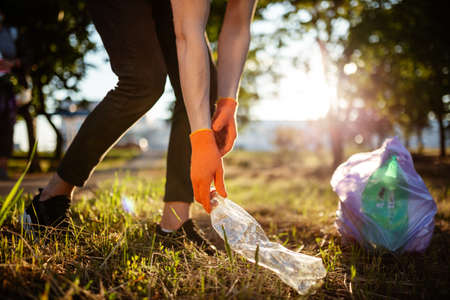 Man picks up litter outdoors, collecting used plastic bottle trash. A volunteer cleans up the park on a sunny bright day. Clearing, pollution, ecology and plastic conceptの写真素材