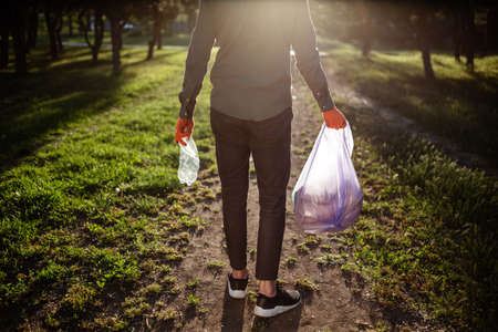 Young man walks with trahs bag and used plastic bottle in his hands.