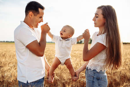 Happy parents hold a child in their arms in a wheat field. A woman and a man play with a child on a sunny summer day. Photo of a happy familyの写真素材