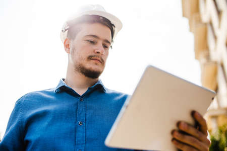 An engineer or an architect in a helmet with a tablet in his hands. Monitoring the progress of construction. A man in a hard hatの写真素材