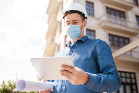 Young architect with the tablet and wearing medical mask checking the details on the construction...