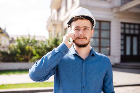 Portrait of young architect in hard hat with smartphone. Engineer talking on the phone on a construction siteの写真素材