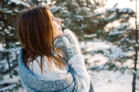 Portrait of a red-haired girl in mittens against the background of a winter park. Beautiful woman is enjoying nature on a snowy dayの写真素材