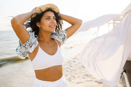 Portrait of a beautiful young woman in a straw hat on the beach against the backdrop of the sea and...